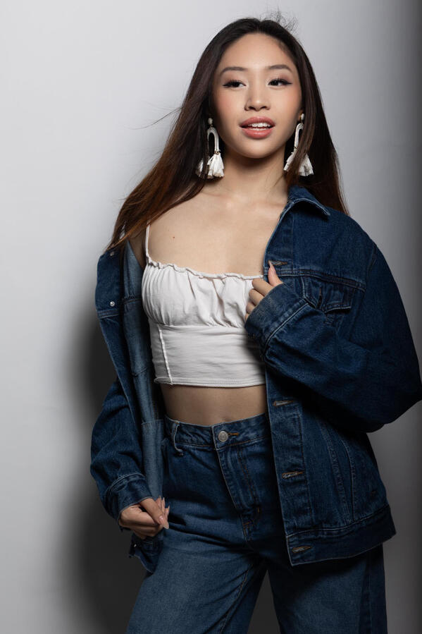 Angeli Chaves smiling in a white crop top and denim set with tassel earrings