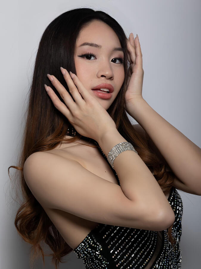Close-up of Angeli Chaves with hands framing her face, wearing a rhinestone halter gown and crystal bracelet