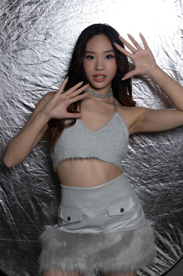Angeli Chaves posing in a fuzzy gray halter top and leather skirt with fur trim in front of a metallic backdrop