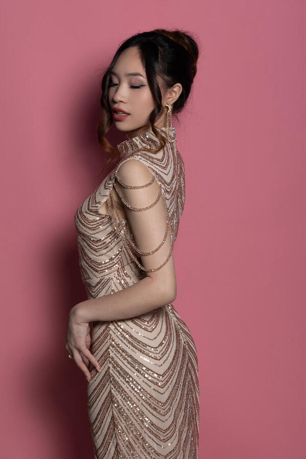 Side view of Angeli Chaves in a champagne sequin gown with beaded shoulder drapes, looking down