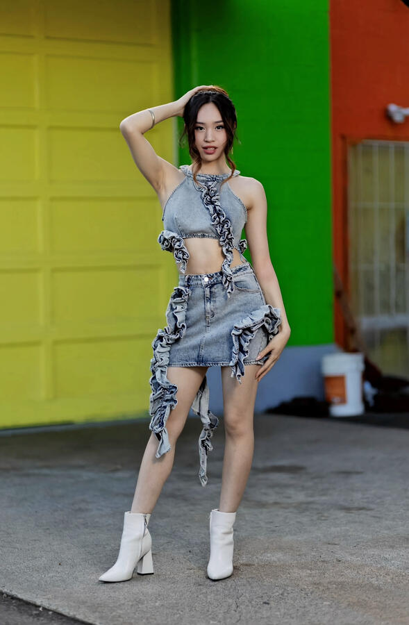 Angeli Chaves standing in front of a colorful wall in a denim ruffle two-piece with one hand on her head